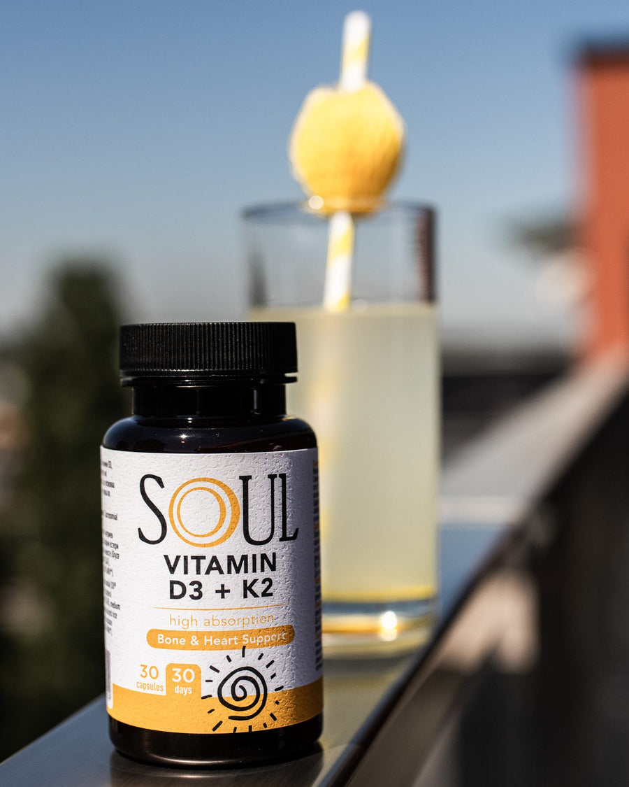SOUL Vitamin D3 + K2 on a balcony ledge beside a glass of lemonade