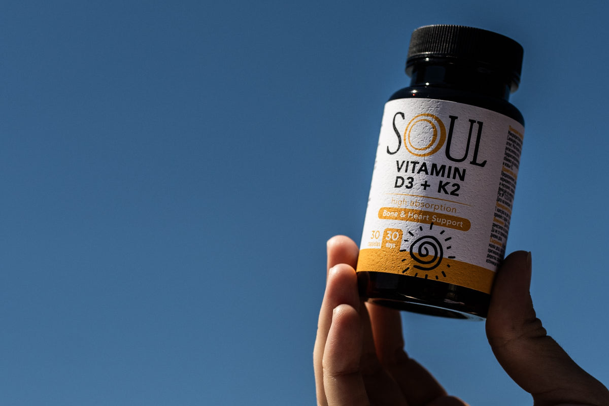 Ръка държи SOUL Vitamin D3 + K2 на фона на ясно синьо небе