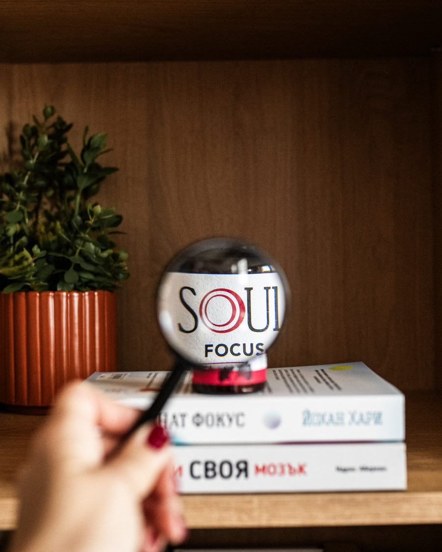 Ръка с лупа пред SOUL Focus върху книги на рафт